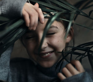 A cheerful child, a charming girl's face looking through the leaf of the plant.