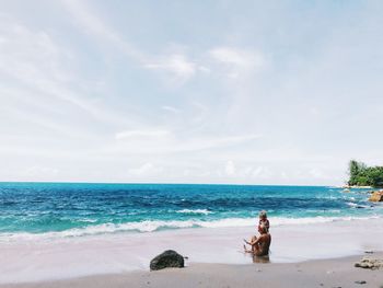 Man sitting on beach against sky