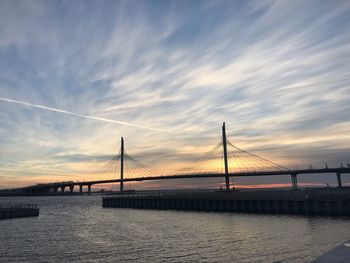 Suspension bridge over sea against sky during sunset