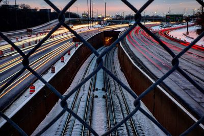 Light trails seen through chainlink fence on road at night