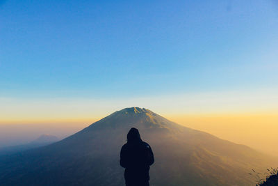 Rear view of silhouette man standing on mountain against sky