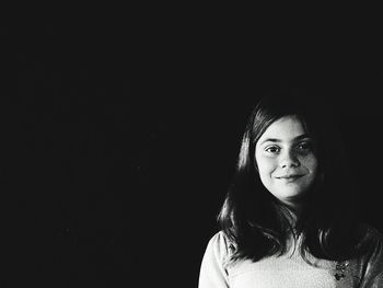 Portrait of smiling young woman against black background