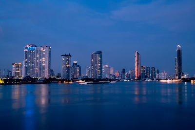 Illuminated buildings in city against blue sky