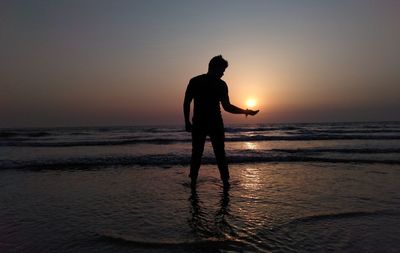 Silhouette man standing on beach against sky during sunset
