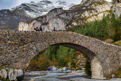 Low angle view of people standing on arch bridge against mountains