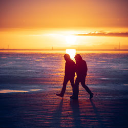 Silhouette men on beach against sky during sunset