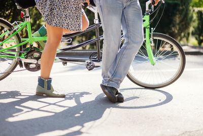 Low section of couple standing with tandem bicycle on road