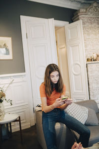 Girl using mobile phone while sitting on sofa at home