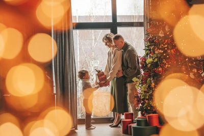 Portrait of happy family in knitted beige sweaters waiting santa indoor.