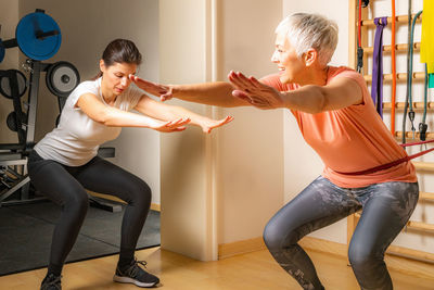 Female fitness instructor instructing mature woman exercising in gym