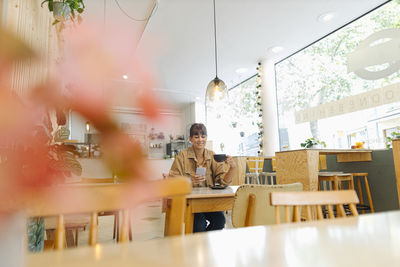 Female entrepreneur text messaging on smart phone holding coffee cup while sitting in cafe