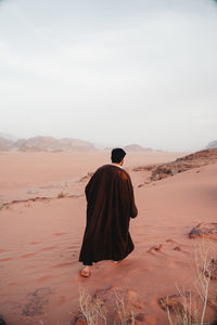 Rear view of man walking at desert against sky