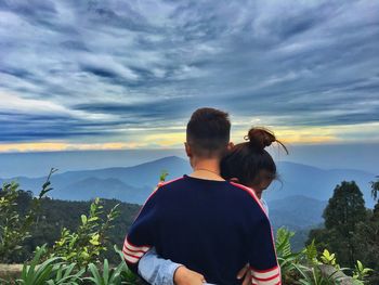 Rear view of friends against cloudy sky