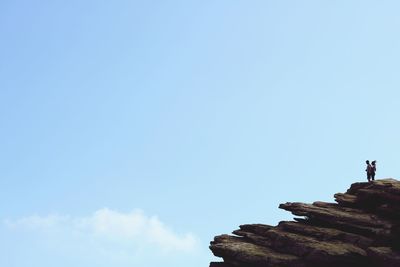 Low angle view of men standing on rock against sky