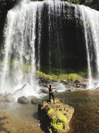 Rear view of woman with arms outstretched looking at waterfall