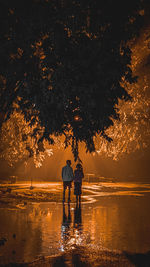 Full length of couple standing by water at park during night
