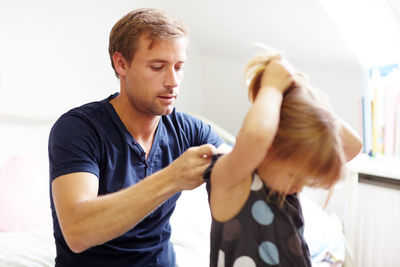 Father helping daughter to wear clothes at home