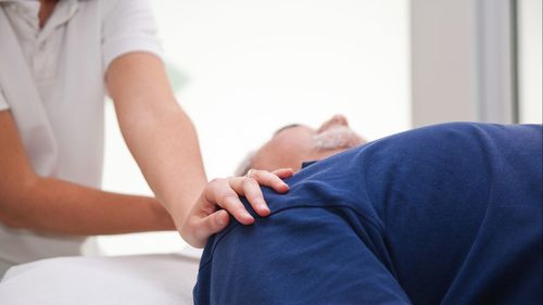 Midsection of man massaging customer shoulder at spa