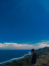 Rear view of man standing on sea against blue sky