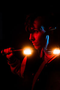 Portrait of young man holding lit candle against black background