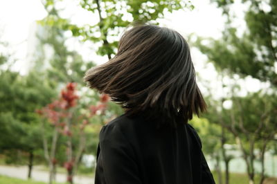 Rear view of woman with tousled hair standing against trees