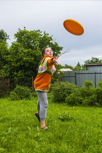 Full length of playful girl throwing plastic disc while standing at yard