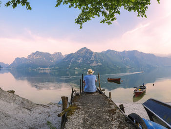 Italy, lombardy, back view of man sitting on jetty at lake idro at morning twilight