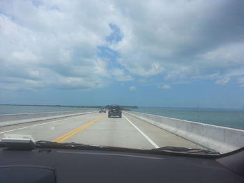 Cars on road against sky seen from car windshield