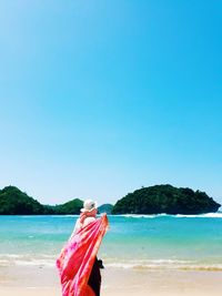 Rear view of woman with scarf standing at beach during sunny day