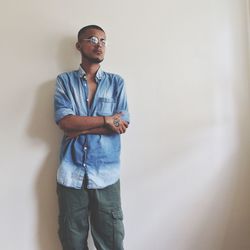 Thoughtful young man standing with arms crossed against wall