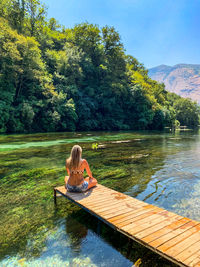 Woman sitting by lake against trees