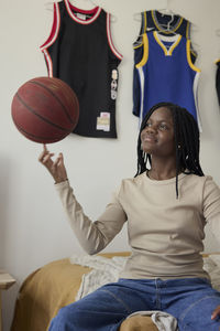 Teenage girl spinning basketball on her finger while sitting in bedroom at home