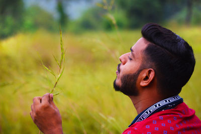 Young man holding plant on field