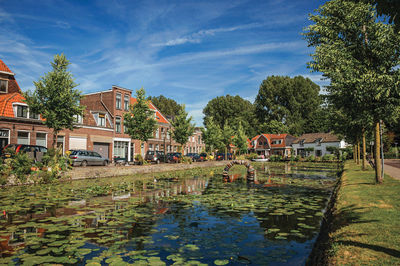 Houses by lake and buildings against sky in city