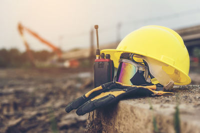 Close-up of yellow hardhat with walkie-talkie and gloves on retaining wall at construction site