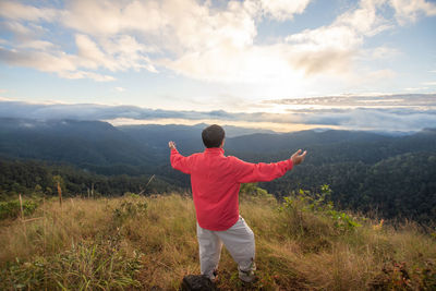 Rear view of carefree man standing on mountain against sky during sunset