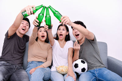 Cheerful friends toasting bottles on sofa during soccer match