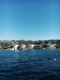 Sea by townscape against clear blue sky