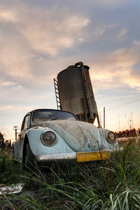 Abandoned car on field against sky during sunset
