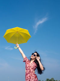 Woman holding umbrella while standing against blue sky