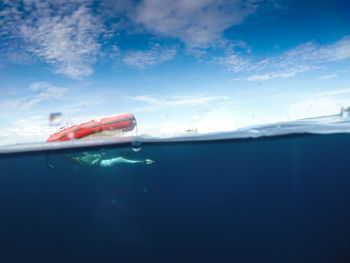 Shirtless man swimming in sea under inflatable raft against cloudy sky