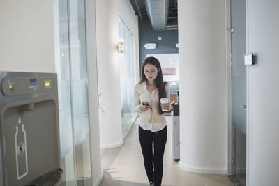 Young woman using phone while standing against door