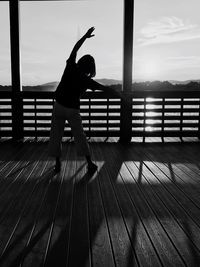 Silhouette woman exercising on floorboard against sky