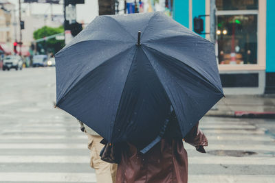 Fashionable young woman walks down a rainy street with a plain blackumbrella and cute brown jacket.