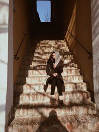 Full length of woman sitting on staircase amidst building