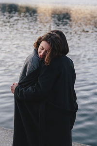 Lesbian couple embracing while standing against river