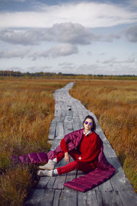 Woman  in red warm clothes and a big scarf on an ecological trail in the autumn not a swamp