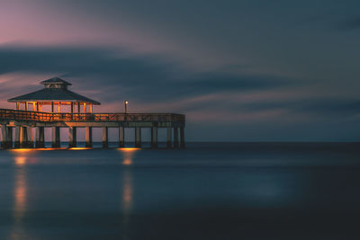 Illuminated built structure over sea against cloudy sky at dusk