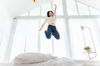 Full length of young woman jumping on bed at home