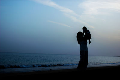 Woman playing with son while standing at beach against sky